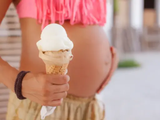 Schwanger und Lust auf Eis? Eine Frau hält eine Eistüte, während sie ihren Bauch streichelt.