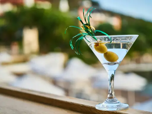 Idealny martini aperitivo z dwiema oliwkami, ozdobiony zielonymi wstążkami, na tle letniego krajobrazu.
