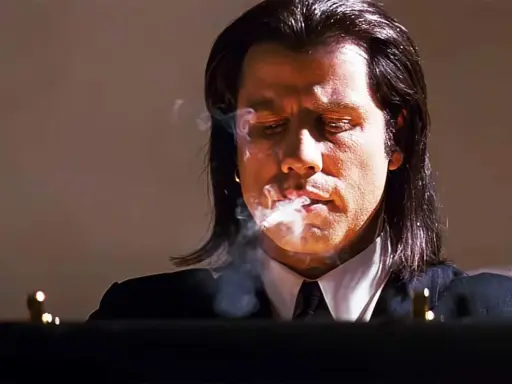 John Travolta i en ikonisk scen från filmer, med rök som virvlar runt hans ansikte.