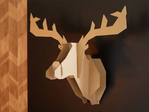 Trophée de cerf stylisé, œuvre de bricolage avec du carton de récupération, accroché sur un mur sombre à côté d'un panneau décoratif en bois.