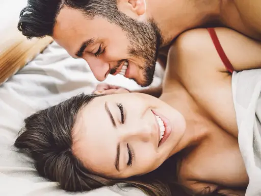 Pareja sonriente en la cama, disfrutando de intimidad.