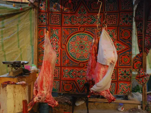 Fleisch hängt vor einem bunten Stoffmuster, bereit für Eid el Adha.