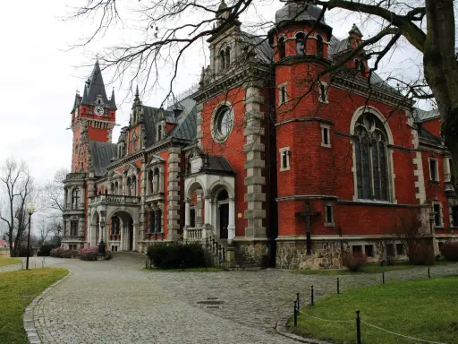 Pławniowice atrakcje: okazały pałac z czerwoną cegłą, wieżą zegarową i brukowanym dziedzińcem.