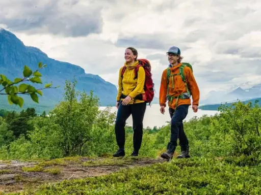 Två glada vandrare med ryggsäckar på en stig i fjällen. En perfekt plats att bo på efter en dag av vandring, kanske på ett STF vandrarhem.