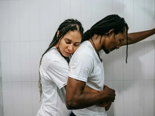 Una pareja se abraza con tristeza, reflejando el momento en que empiezan los problemas de pareja. Él se apoya en la pared, ella recuesta su cabeza en su hombro.