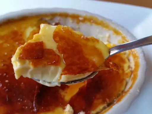 En sked lyfter en bit krämig creme brulee med knäckig karamelliserad yta.