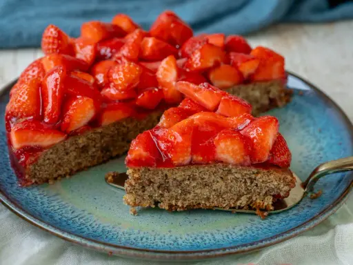 Ein saftiger, glutenfreier Erdbeerkuchen mit frischen Erdbeeren und glänzender Tortenglasur auf einem blauen Teller.