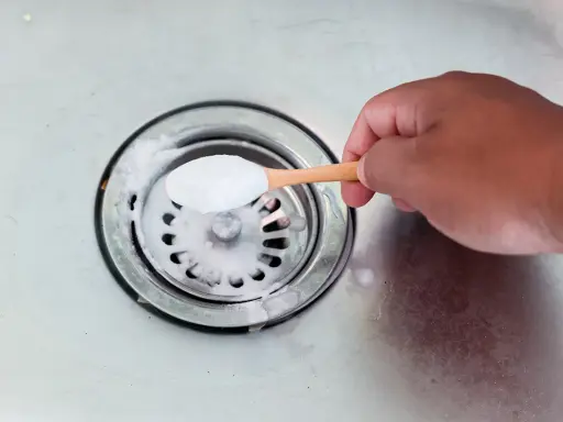 Maintenant, je vais aider à déboucher le siphon. Une cuillère de bicarbonate de soude est versée dans l'évier.