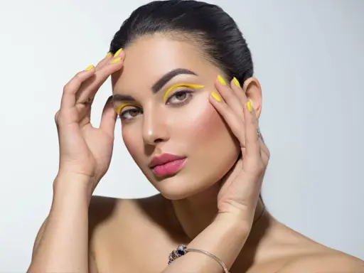 Mujer con un atrevido doble eyeliner amarillo y uñas a juego.