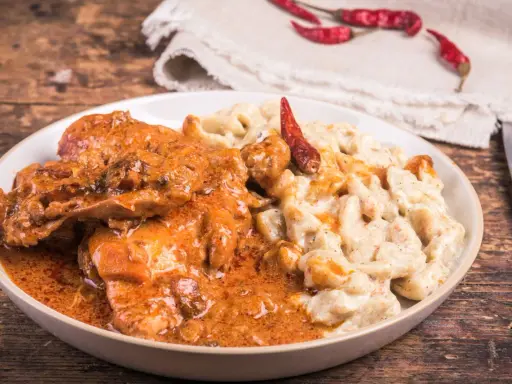 Gulasz z warzywami, podany z kremowym sosem i ozdobiony suszonymi papryczkami chili, kusi apetycznym wyglądem.