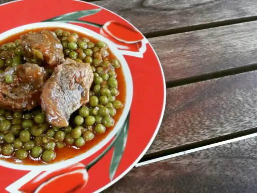 Un saporito spezzatino con piselli, servito su un piatto rosso decorato con tulipani, pronto per essere gustato.