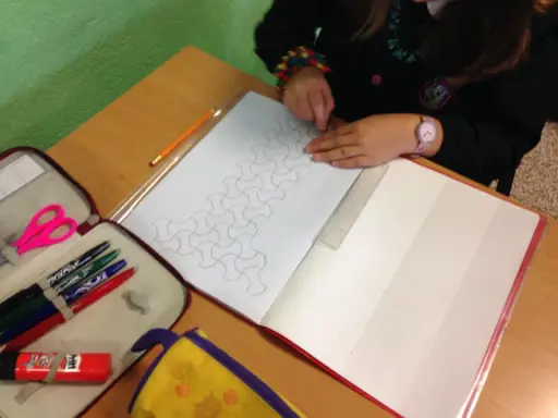 Bambina disegna un motivo geometrico su un quaderno di matematica. Matite, forbici e righello a portata di mano.