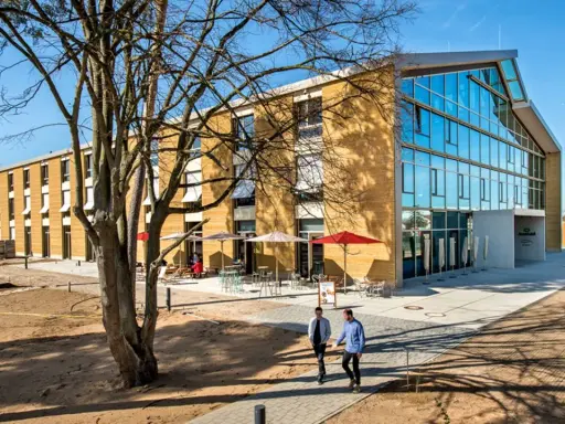 Modernes Gebäude mit Glasfront und Fassade aus nachhaltigen Materialien. Zwei Männer gehen auf einem Weg.