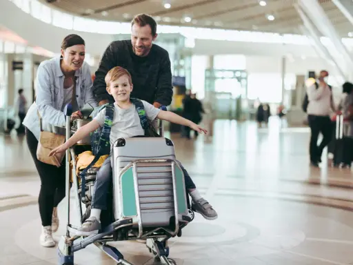 Familj på flygplatsen med ett barn sittandes på handbagage. De är glada och redo för sin resa.