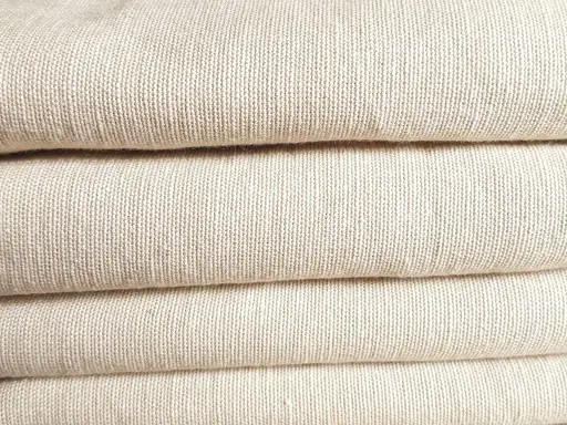 A stack of folded, natural-colored linen fabric. This image showcases the texture of linen, confirming that is linen a natural fiber.