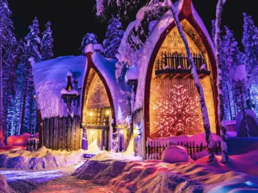 Noche mágica en Finlandia con niños. Casas nevadas iluminadas con luces de colores, rodeadas de árboles cubiertos de nieve.