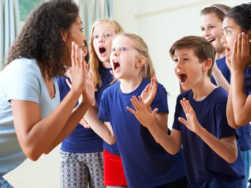 Bambini entusiasti in cerchio, con la maestra che guida attività di psicomotricità e linguaggio, stimolando espressioni vocali e corporee.
