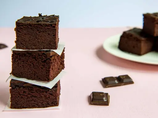 Ciemne, wilgotne brownie z fasoli, ułożone w wieżę, obok kawałków czekolady.