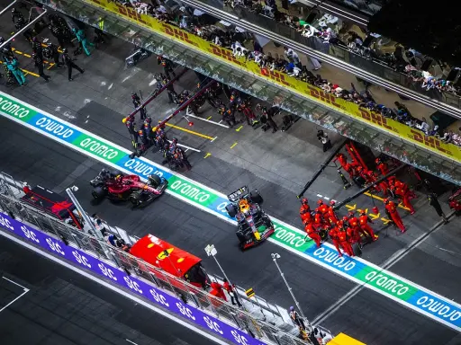 Equipos de F1 en boxes. Un coche Red Bull con un undercut f1 se detiene, mientras mecánicos de Ferrari se preparan.