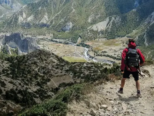 Widok z góry na dolinę i góry. Turysta z plecakiem zastanawia się, co zabrać w góry.