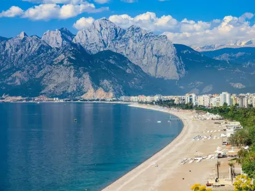 Ein malerischer antalya strand mit türkisfarbenem Wasser, weißen Bergen im Hintergrund und einer Stadtkulisse.