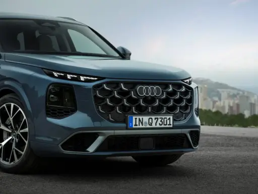 Przód eleganckiego Audi Q7 3.0 TDI w kolorze granatowym, z charakterystycznym grillem i światłami LED, na tle miejskiego krajobrazu.