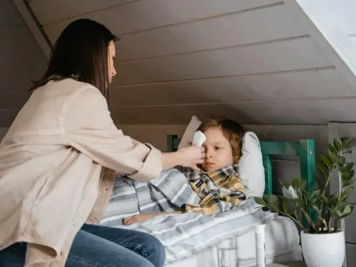 Mama mierzy gorączkę choremu dziecku, szukając domowych sposobów na zapalenie krtani u dziecka.
