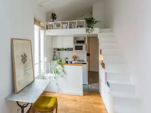 Un petit appartement optimisé avec un coin cuisine, un bureau escamotable et un escalier menant à une mezzanine. Idéal pour un **DIY rangement** créatif.