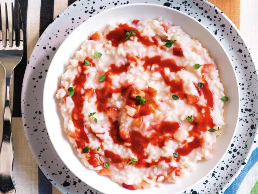 Un cremoso risotto alle fragole, guarnito con salsa di fragole e foglioline verdi, pronto per essere gustato.