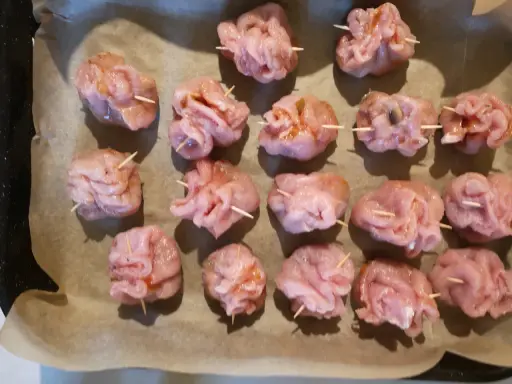 Gotowe do pieczenia sakiewki ze schabu, ułożone na papierze do pieczenia.