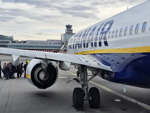 Ryanair-plan på marken med passagerare som väntar. Man undrar om man måste skriva ut boardingkort Ryanair. Flygledartorn i bakgrunden.