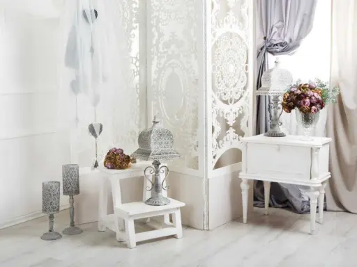 Delikatny salon w stylu shabby chic. Białe meble, ażurowa parawan, świeże kwiaty i ozdobne latarenki tworzą romantyczny nastrój.
