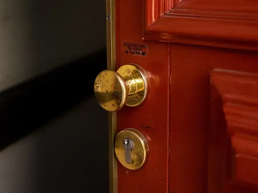 Poignée et serrure dorées sur une porte rouge. Une étiquette indique un service de serrurerie, utile en cas de porte forcée, pour l'assurance propriétaire ou locataire.