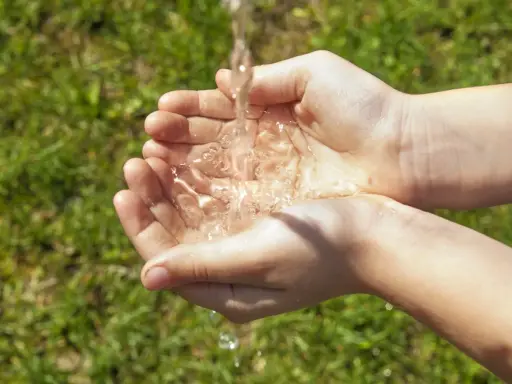 Mains d'enfant recevant un filet d'eau, une façon simple de rendre l'eau moins calcaire pour un usage quotidien.