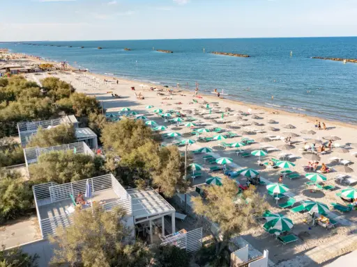 Lidi ferraresi: una distesa di ombrelloni verdi e bianchi sulla sabbia dorata, con il mare azzurro e alcune persone che si godono il sole.