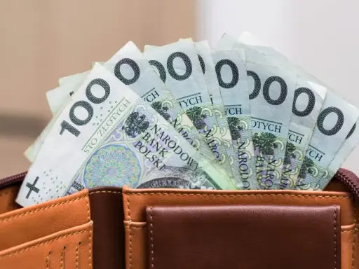 Pieniądze z wesela na konto: stos banknotów po 100 zł w brązowym portfelu.