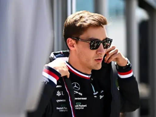 George Russell ajustándose la chaqueta, con gafas de sol y el logo de Mercedes.