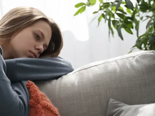 En ung kvinna med utmattningssyndrom symtom vilar på en soffa, ser trött och nedstämd ut.