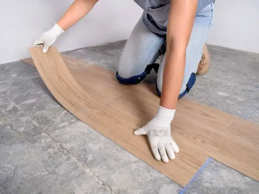 Manos enguantadas colocando suelo vinílico imitación madera sobre suelo de cemento.