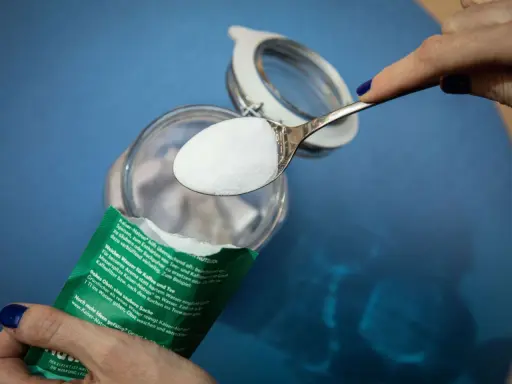 Ein Löffel Natron wird über ein Glas gehalten. Ein natürliches Hausmittel zur Geruchsneutralisierung und Reinigung.