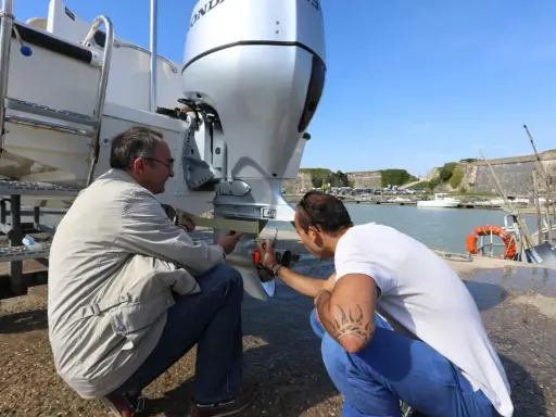 Deux hommes vérifient le montage moteur hors bord sur tableau arrière d'un bateau, près d'un port.