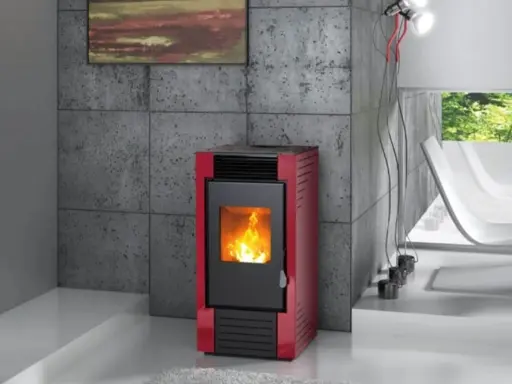 Estufa de pellets roja con fuego encendido, instalada en un salón moderno con pared de hormigón y ventana al exterior.