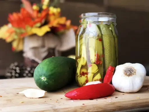 Słoik z ogórkami z chili w plastrach, obok świeży ogórek, czosnek i papryczka chili.
