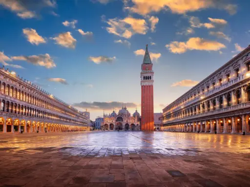 Le **place Saint-Marc à Venise** s'illumine sous un ciel de fin de journée. La basilique et le campanile se dressent majestueusement.