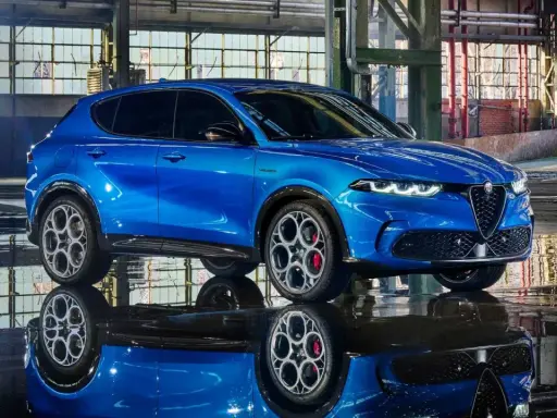 Alfa Romeo Tonale blu, un esempio di stellantis auto elettriche, riflette sul pavimento bagnato di un capannone industriale.