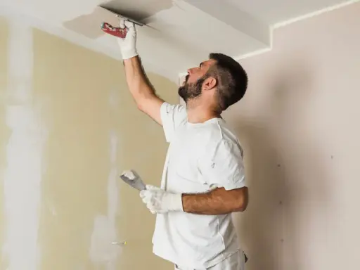 Hombre aplica mortero sobre techo pintado. Se puede aplicar mortero sobre pintura para reparaciones.