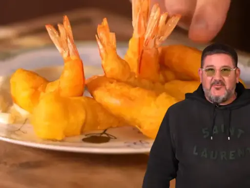 Un hombre sonriente muestra un plato de gambas a la gabardina doradas y crujientes, listas para disfrutar.