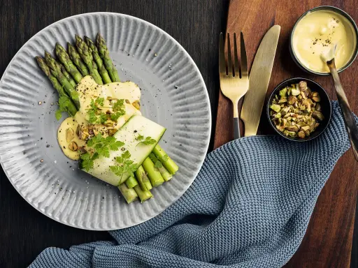 Une belle recette d'asperges vertes, nappées d'une sauce crémeuse et garnies de pistaches concassées. Un délice visuel et gustatif.