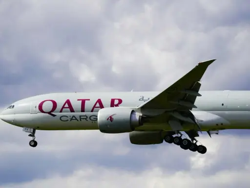 Samolot Qatar Airways Cargo z wysuniętym podwoziem, gotowy do lądowania. W tle chmury.