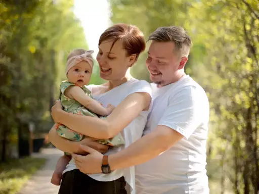 Szczęśliwa rodzina z córeczką w letnim parku. Mama tuli dziecko, tata obejmuje ich. Idealne babciowe warunki na spacer.